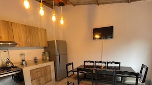 Una cocina con armarios de madera, piso de mármol, una mesa de comedor con sillas, un refrigerador y un televisor montado en la pared.