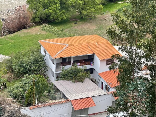 A two-story house with a red-tiled roof, a balcony on the upper floor, and a small garden area.