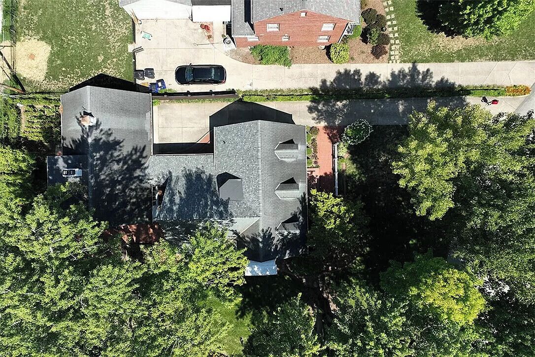 Una vista aerea di una zona residenziale con una casa caratterizzata da un originale design del tetto geometrico, immersa nel verde e con un vialetto pulito.
