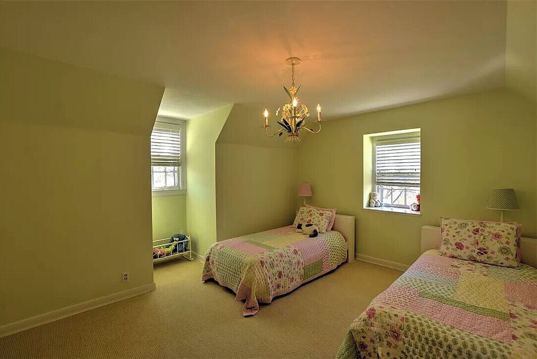 Quarto com duas camas, um candelabro e duas janelas com persianas.