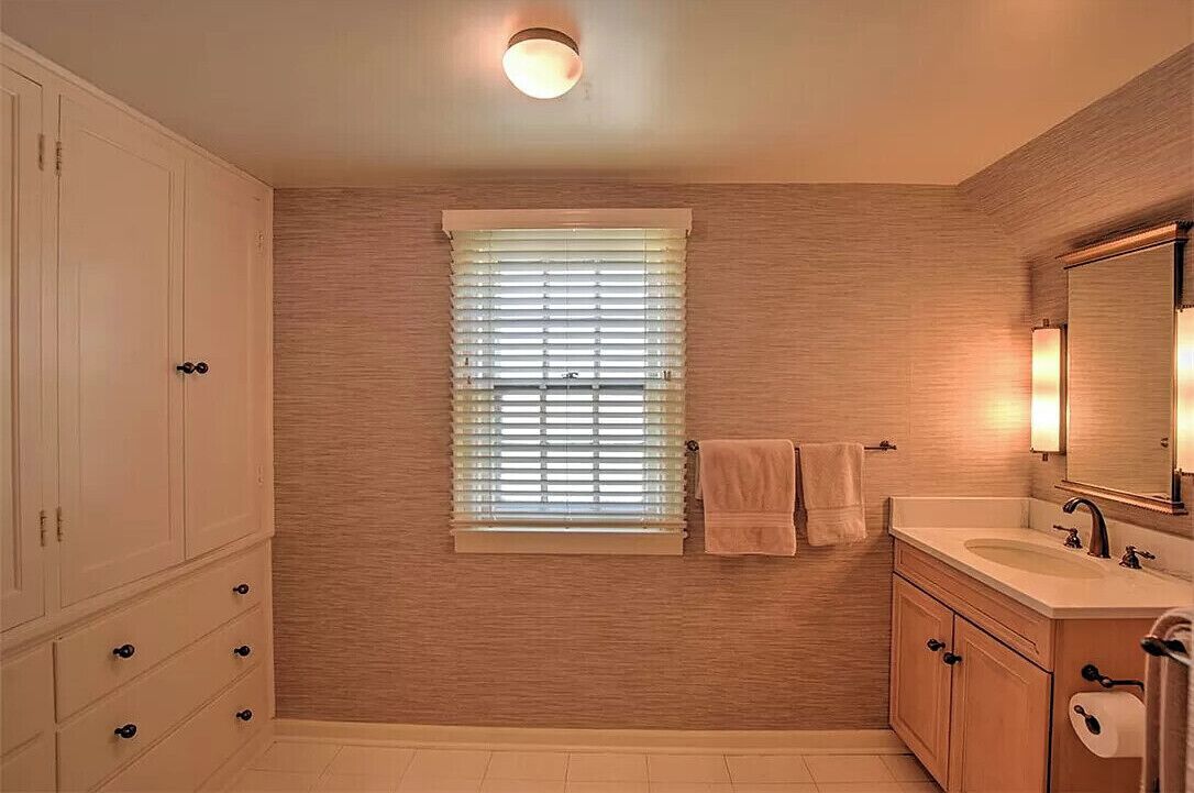 Un baño con ventana, lavamanos, espejo y armarios de madera.
