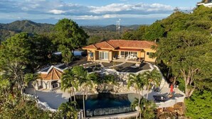 A resort with a swimming pool, palm trees, and a view of the surrounding hills. - Stunning Mountaintop Property with Stylish Main Home, Private Guesthouse & Infinity Pool (Potrero)
