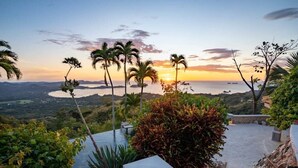 A scenic view of a coastal landscape with palm trees and a sunset. - Stunning Mountaintop Property with Stylish Main Home, Private Guesthouse & Infinity Pool (Potrero)