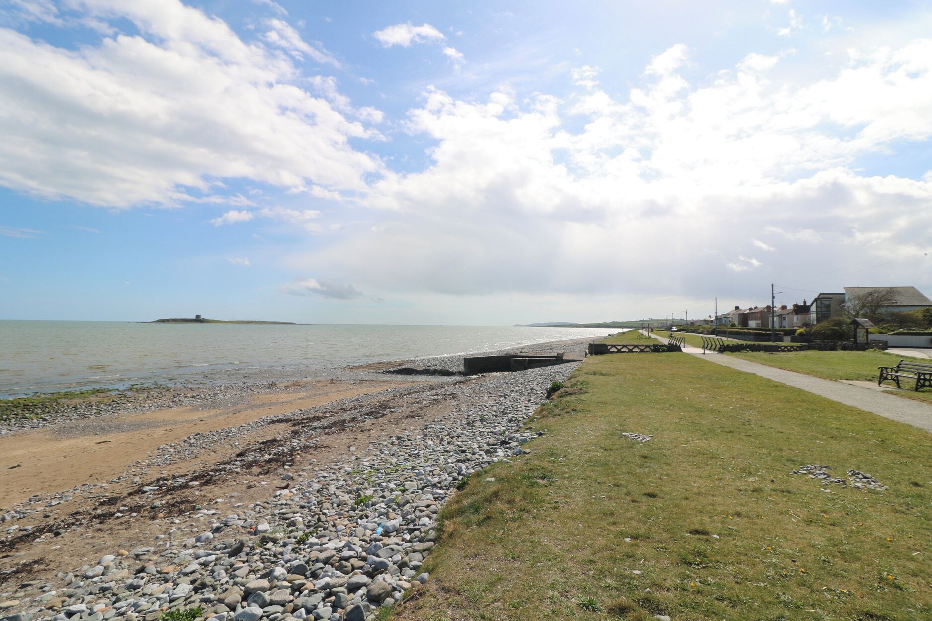 Een kustlandschap met een kiezelstrand, een grasveld en een eiland in de verte.