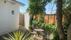 A small patio area with a tiled table and chairs, surrounded by plants and a wooden fence. - To The Beach! (Skerries)