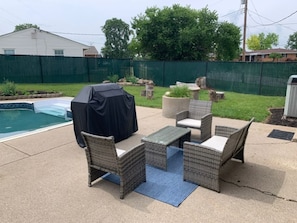 Een terras buiten met rieten meubilair, een overdekte barbecue en een zwembad.