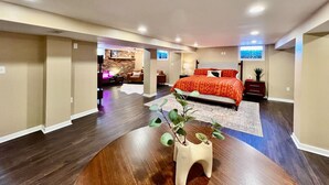 A spacious bedroom with a large bed, a wooden floor, and a view of a cityscape through a window. - All the Vibes Poolside in Trenton! (Trenton)