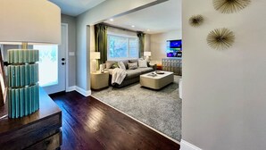 A living room with a sofa, coffee table, and a TV. There is a door leading to another room. - All the Vibes Poolside in Trenton! (Trenton)