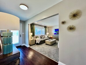 Ein Wohnzimmer mit einer Couch, einem Couchtisch und einem Fernseher. Eine Tür führt in einen weiteren Raum.