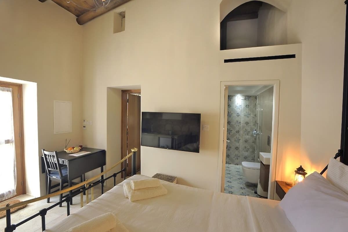 Un dormitorio con cama, escritorio, silla, televisor y baño.