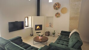 A living room with a fireplace, green sofas, a flat-screen TV, and decorative wall art. - Pentasino Heritage Suites (Agios Theodoros)
