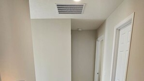 Un couloir avec un bureau blanc, une lampe de bureau noire et un panier rempli d’objets.