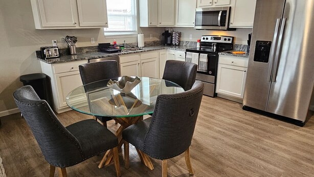 Une cuisine moderne avec des meubles blancs, un réfrigérateur en acier inoxydable, une table à manger en verre avec des chaises, et un four à micro-ondes placé au-dessus de la cuisinière.