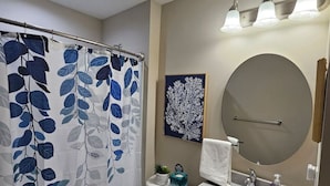 A bathroom with a shower curtain, toilet, sink, and a large mirror. - Cozy Charming Cottage-Style Home (Hamilton)