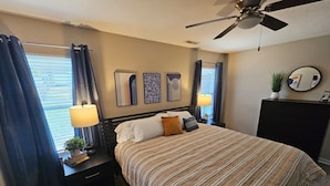 A bedroom with a bed, bedside tables, a ceiling fan, and artwork on the wall. - Cozy Charming Cottage-Style Home (Hamilton)
