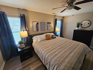 A bedroom with a bed, bedside tables, a ceiling fan, and artwork on the wall.