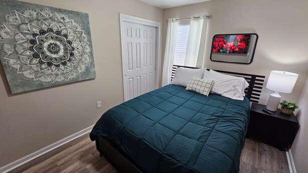 Une chambre à coucher comprenant un lit, une table de chevet, un téléviseur fixé au mur, une porte et une grande œuvre d’art décorative.