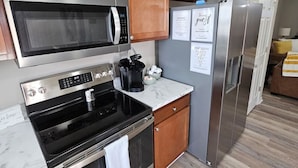 A modern kitchen with wooden cabinets, stainless steel appliances including a microwave, oven, and refrigerator, and a marble countertop. - Cozy Charming Cottage-Style Home (Hamilton)
