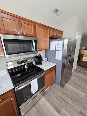 A modern kitchen with wooden cabinets, stainless steel appliances including a microwave, oven, and refrigerator, and a marble countertop.