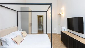 A modern hotel room with a bed, a TV, and a bathroom visible through an open door.
