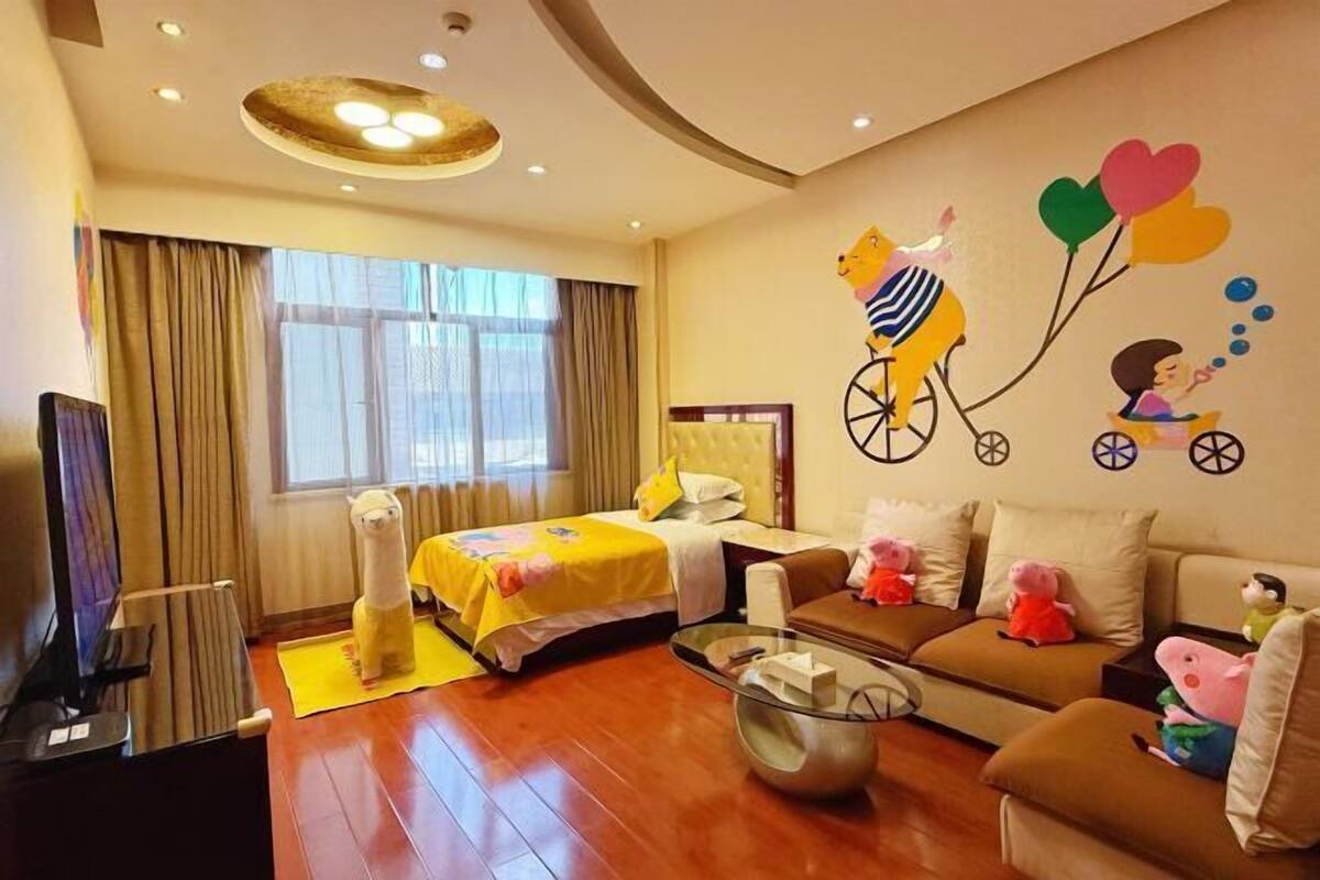 A hotel room with a bed, a sofa, a TV, and a wall with a cartoon character.
