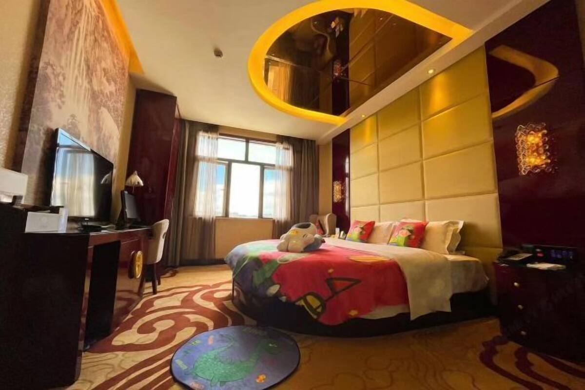 A hotel room with a curved ceiling, a bed with colorful bedding, a desk with a lamp, and a globe on the floor.