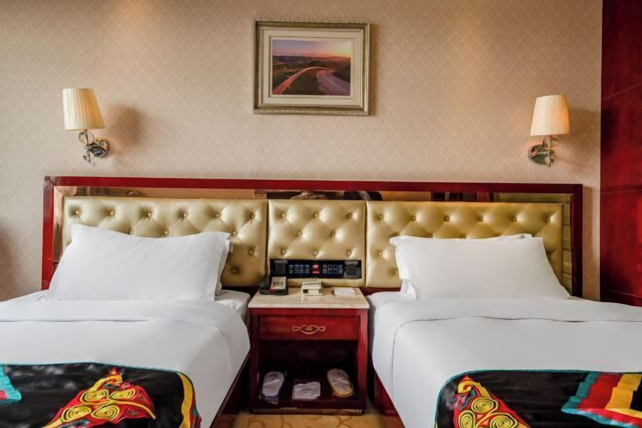 A hotel room with two beds, a headboard with a control panel, bedside lamps, a framed picture on the wall, and a shoe rack.
