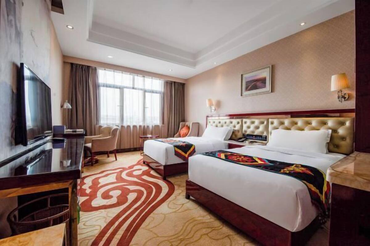 A hotel room with two beds, a TV, a desk, and a large window.