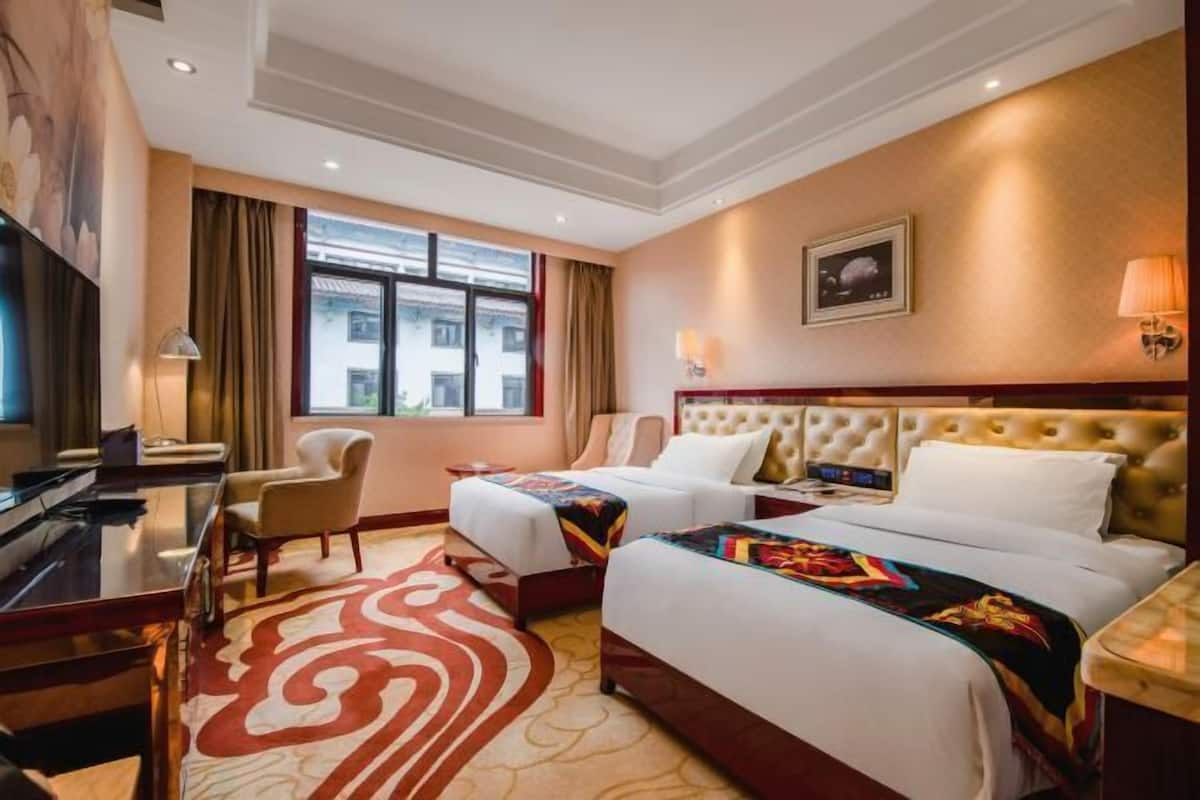A hotel room with two beds, a desk, a TV, and a large window.
