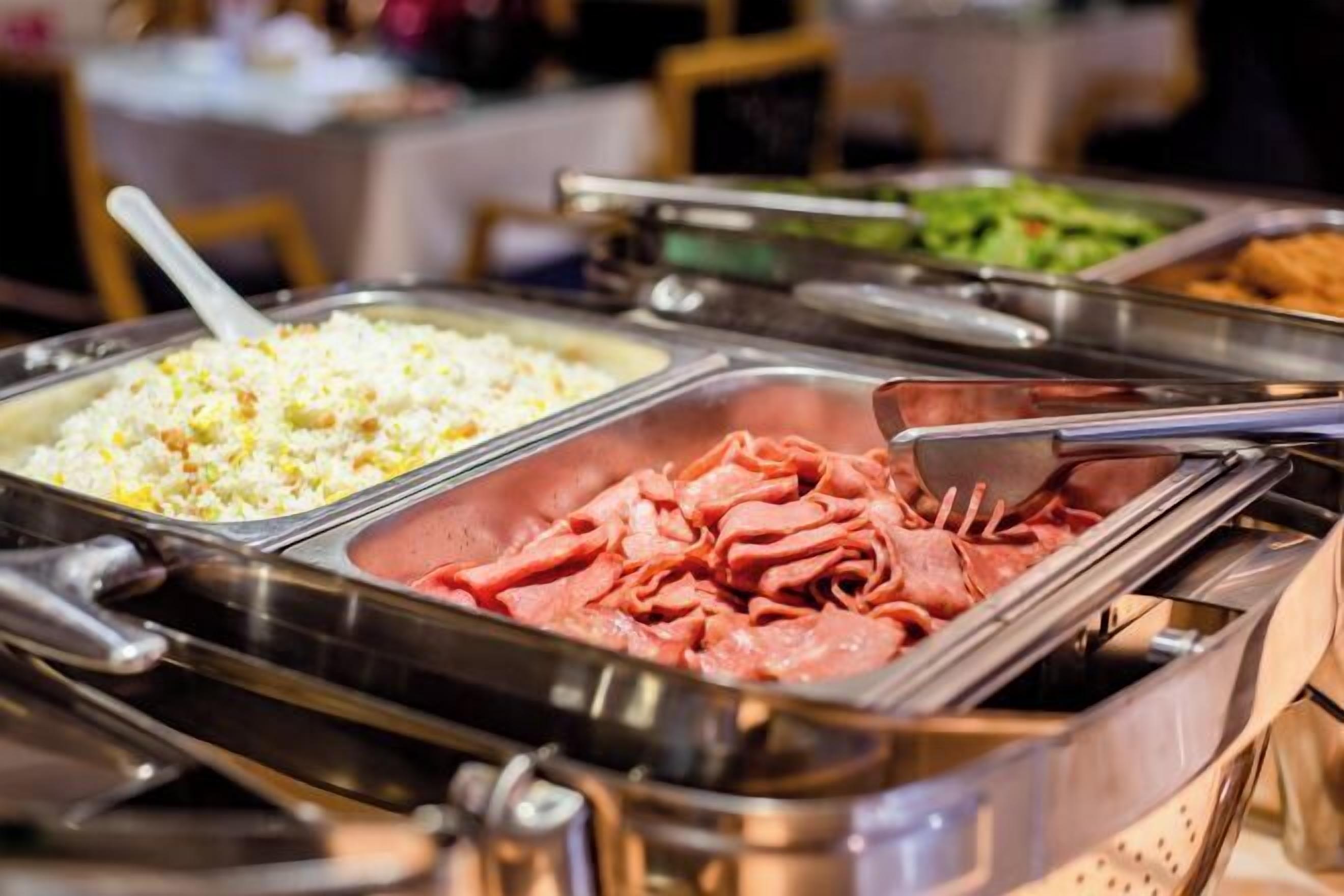 Ein Buffet mit verschiedenen Speisen, darunter Reis, Fleisch und Salate.