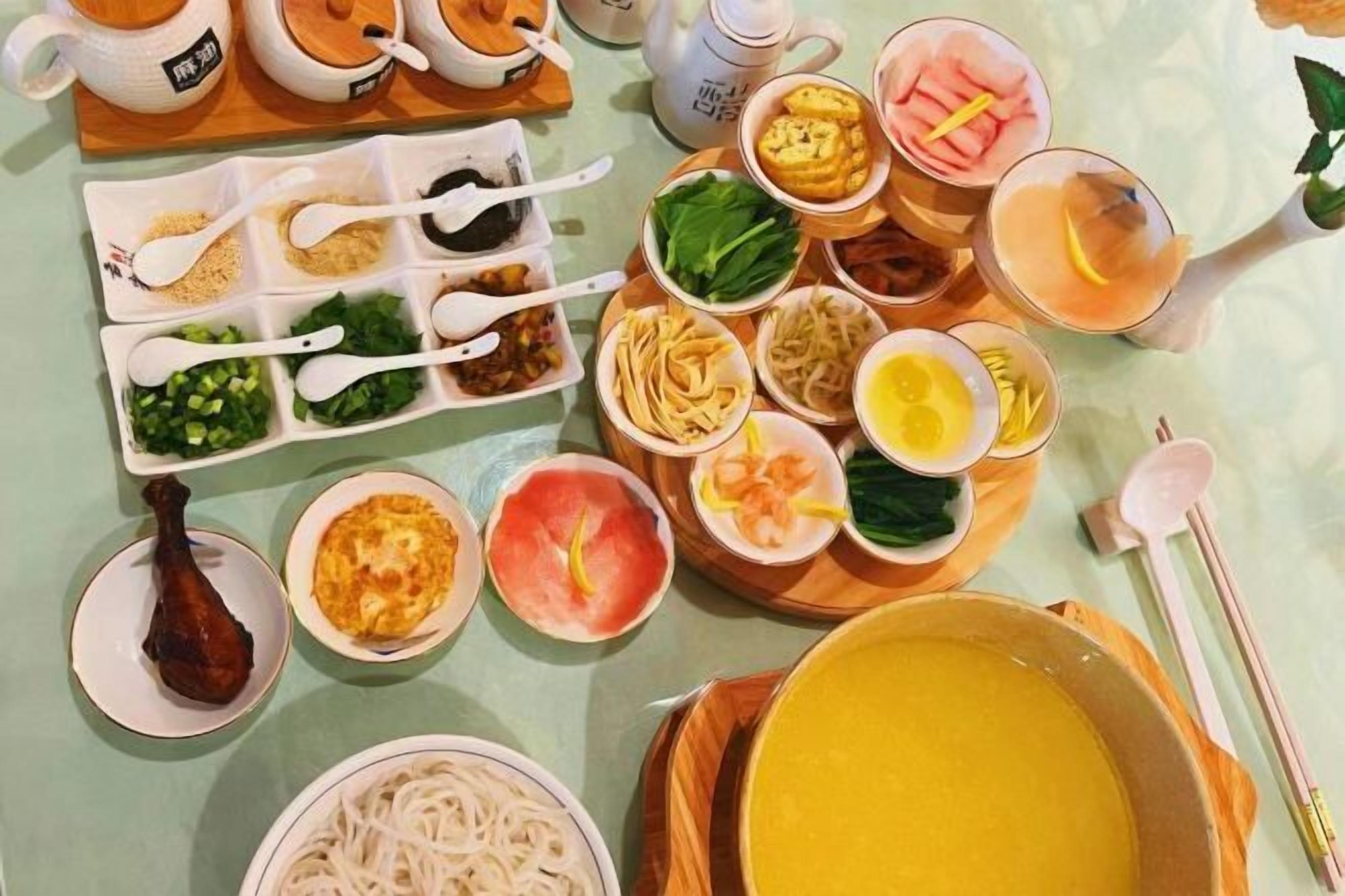 A table with various dishes, including a bowl of soup, plates of noodles, and several small bowls with different ingredients.