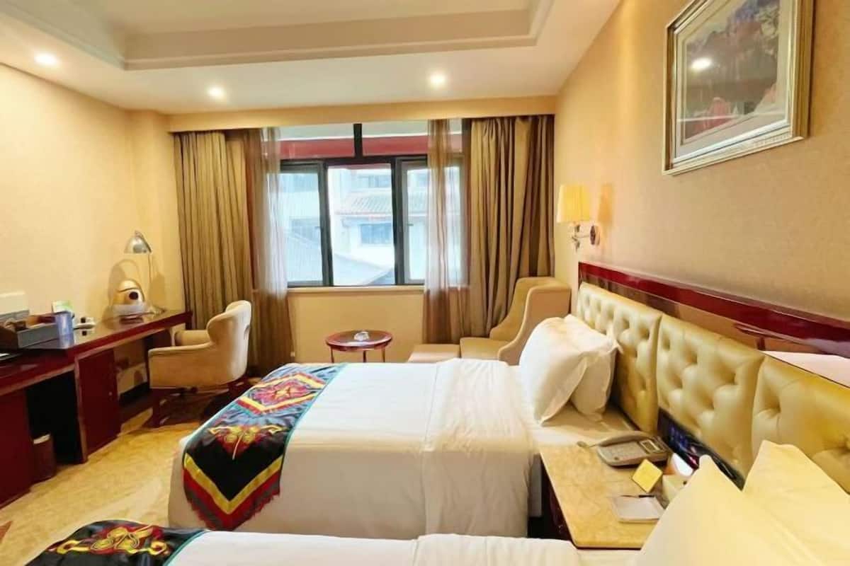 A hotel room with a bed, a desk, a chair, a small table, and a window with curtains.