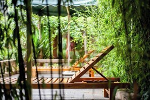 Un fauteuil de relaxation en bois, doté d’une structure métallique, est placé sur un sol en béton, avec une rambarde métallique en arrière-plan.