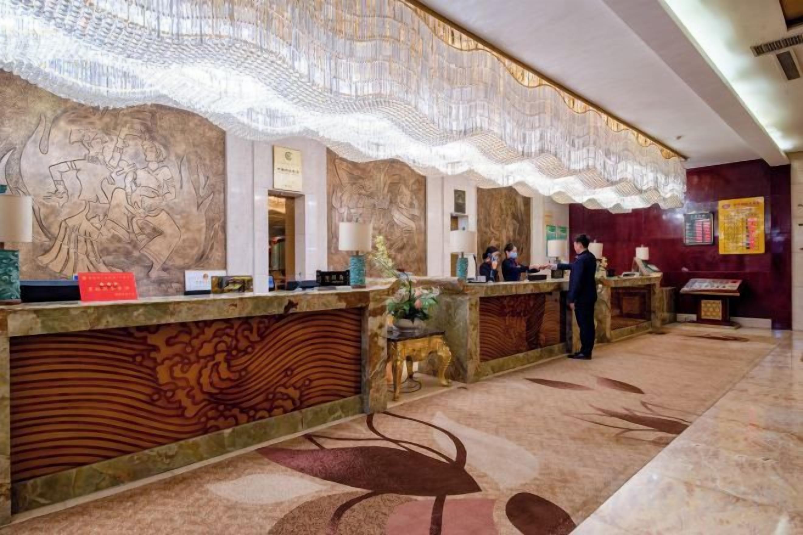 Un hall d’accueil d’hôtel avec un sol en marbre, des décorations murales élaborées et un comptoir de réception.