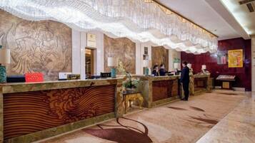 Un hall d’accueil d’hôtel avec un sol en marbre, des décorations murales élaborées et un comptoir de réception.