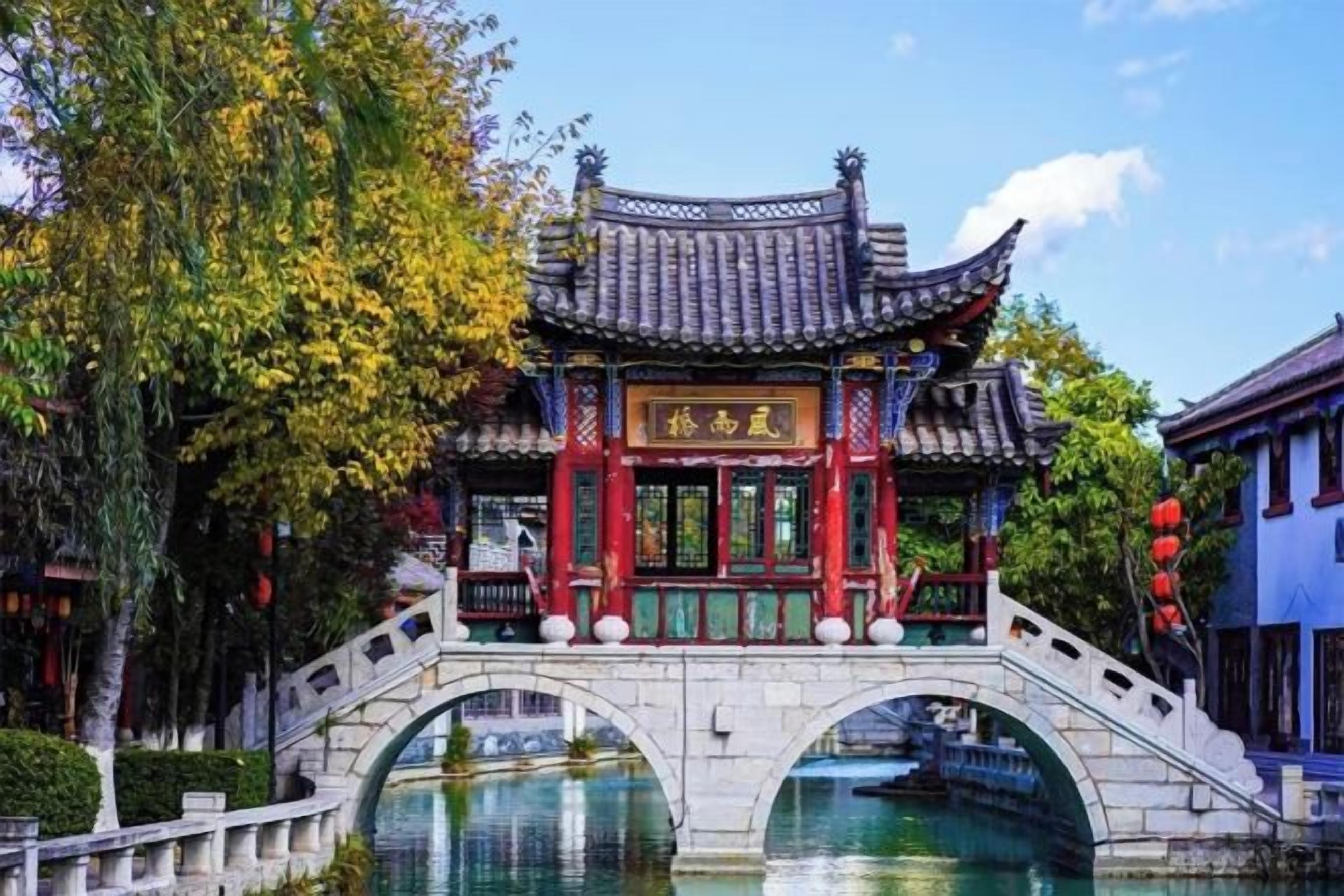 A traditional Chinese pavilion with a tiled roof, a stone bridge, and a clear sky.