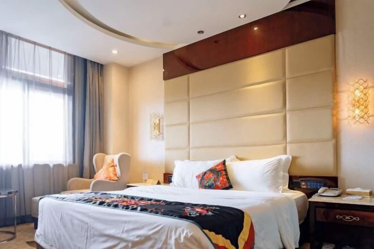 A hotel room with a large bed, a chair, a desk, and a nightstand.