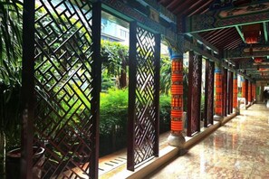 Un couloir agrémenté de panneaux et de colonnes en bois décorées, menant à l’entrée d’un bâtiment.