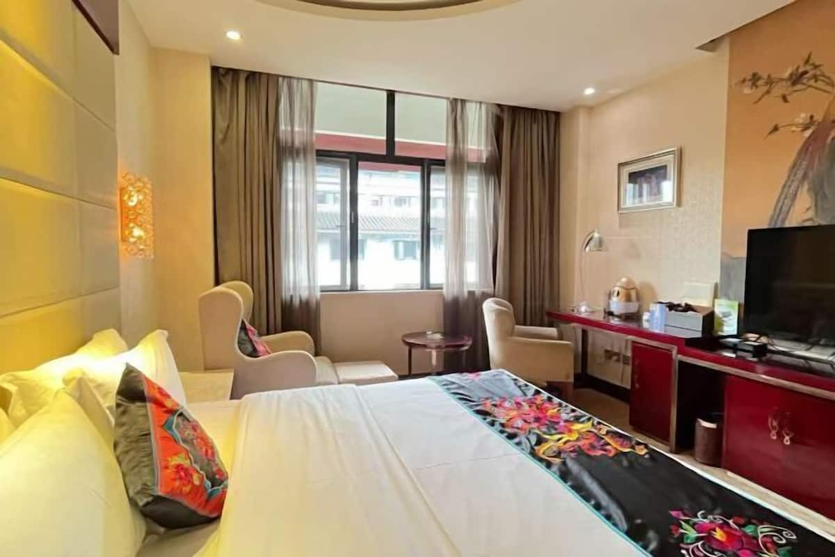 A hotel room with a bed, a desk, a chair, a television, and a window with curtains.