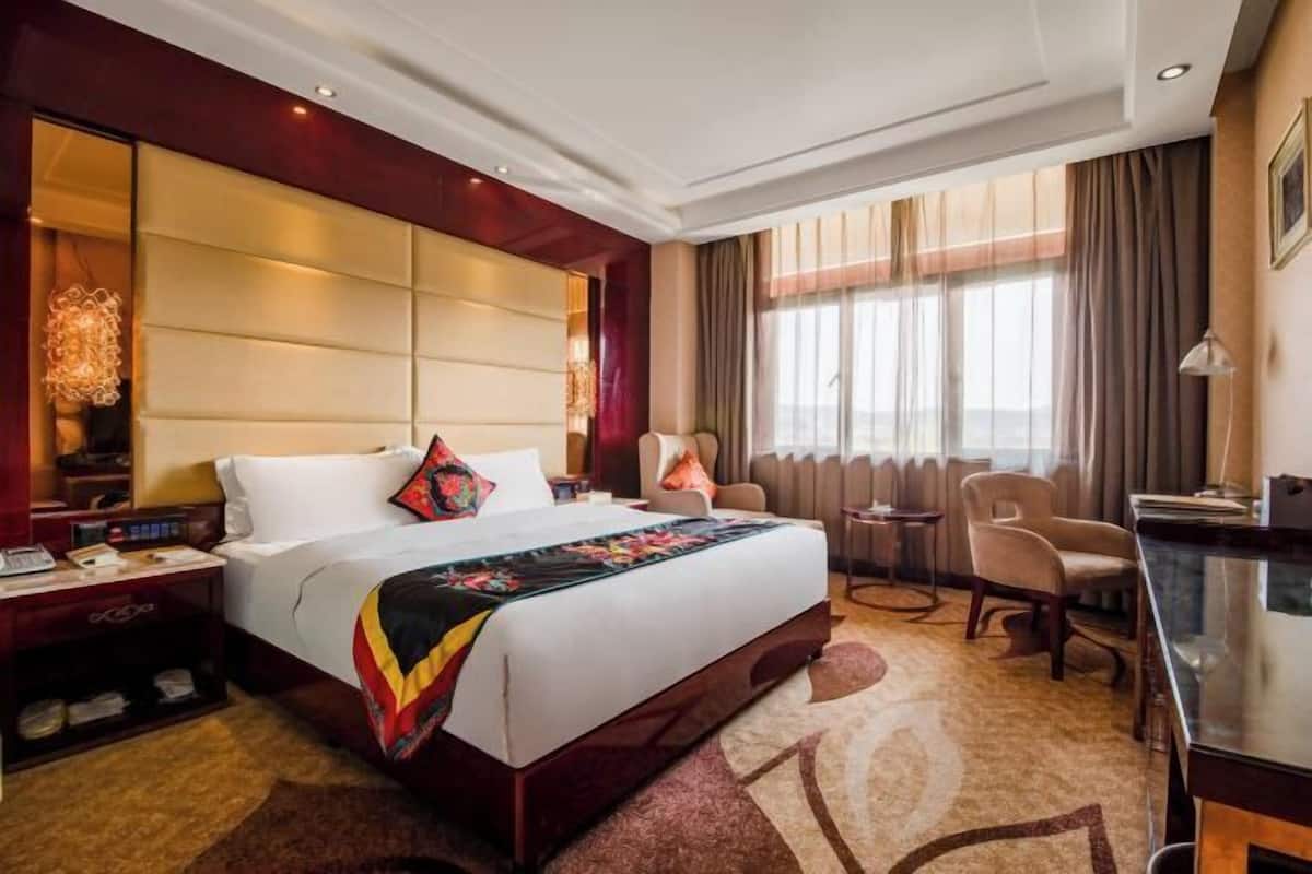 A hotel room with a large bed, a desk, a chair, a nightstand, and a window with curtains.