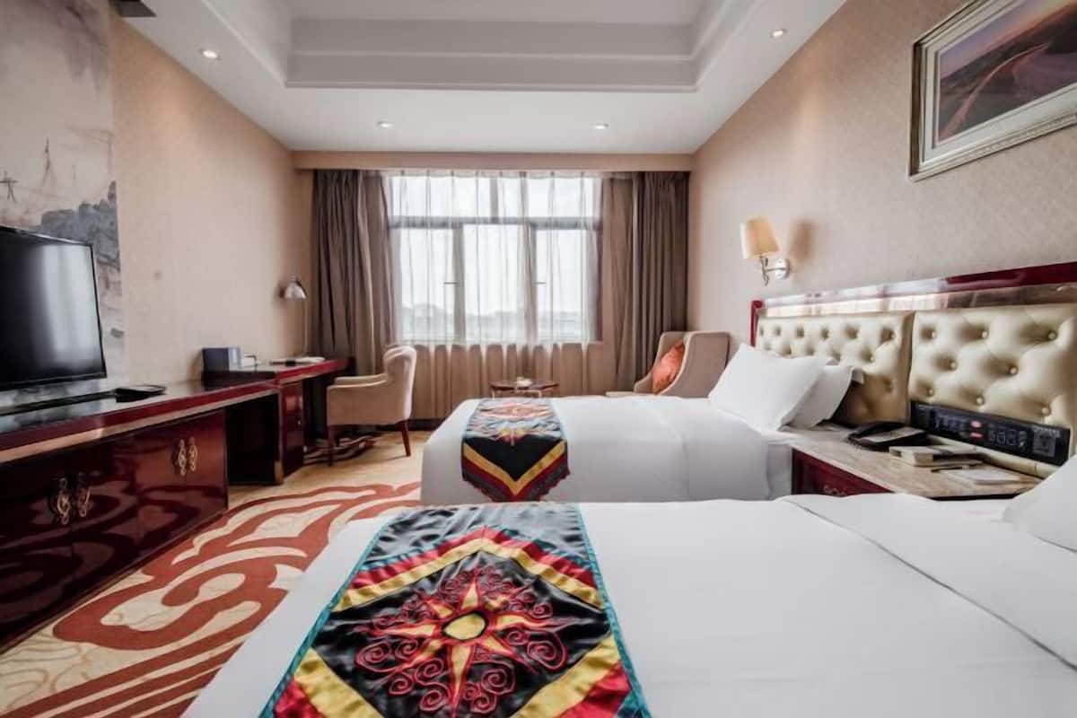 A hotel room with a bed, a TV, a desk, a chair, and a window with curtains.