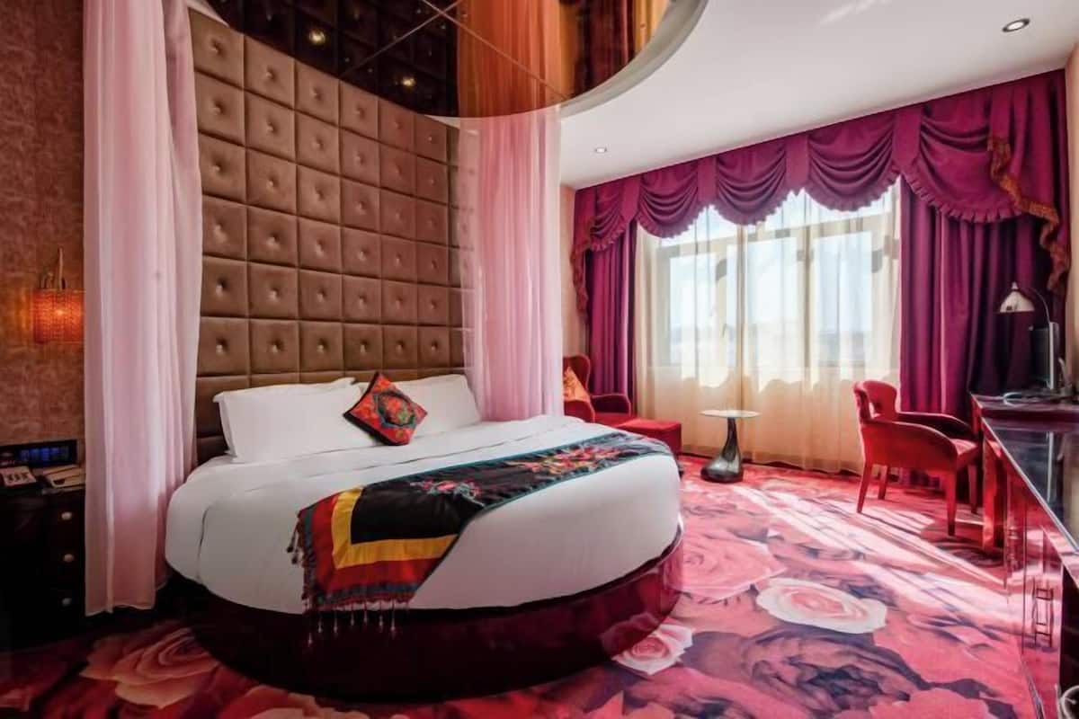 A modern hotel room with a tufted headboard, a large bed, a desk, and a chair.