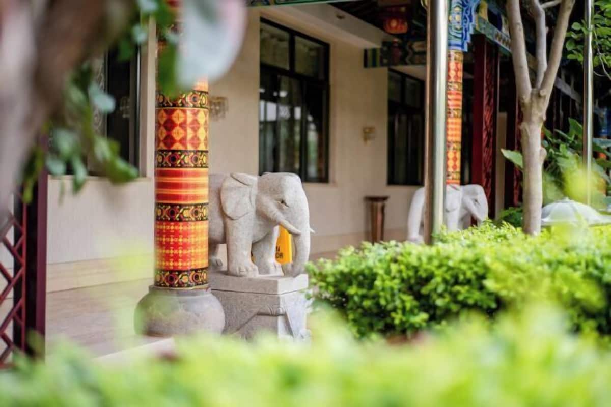 A stone elephant statue in a courtyard with a patterned pillar and greenery.