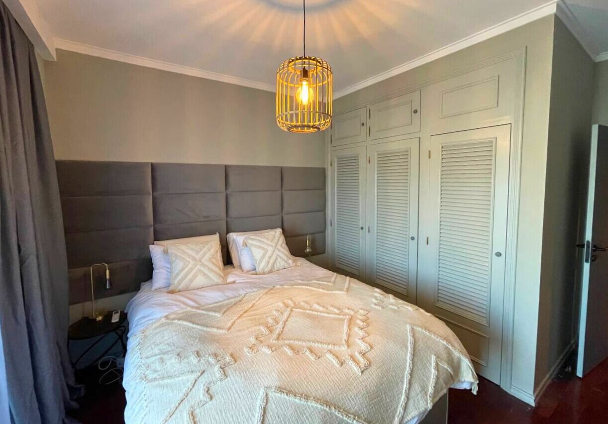 A bedroom with a large bed, a headboard, a hanging light fixture, and a wardrobe.
