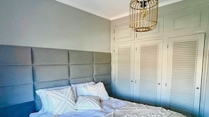 Une chambre à coucher avec un grand lit, une tête de lit, une armoire et un luminaire suspendu.