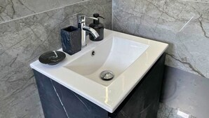 Une salle de bain avec un lavabo blanc, des carreaux de marbre noir et un distributeur de savon noir.