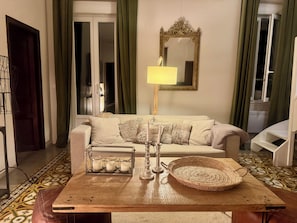 A living room with a sofa, a lamp, a mirror, a tray with candles, and a patterned floor.