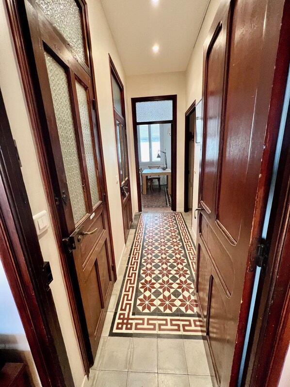 A hallway with patterned floor tiles, wooden doors, and a view into a room with a table and chairs.