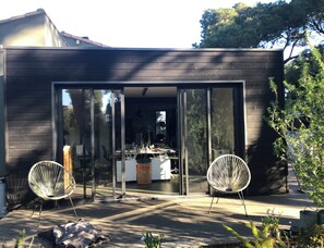 A modern house with a large sliding glass door leading to an outdoor area with two white chairs and a table. - The Maison du Saint Clair in Sète, with its large Mediterranean garden (Sète)