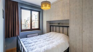 Un dormitorio con cama, ventana con cortinas, radiador y armario de madera.